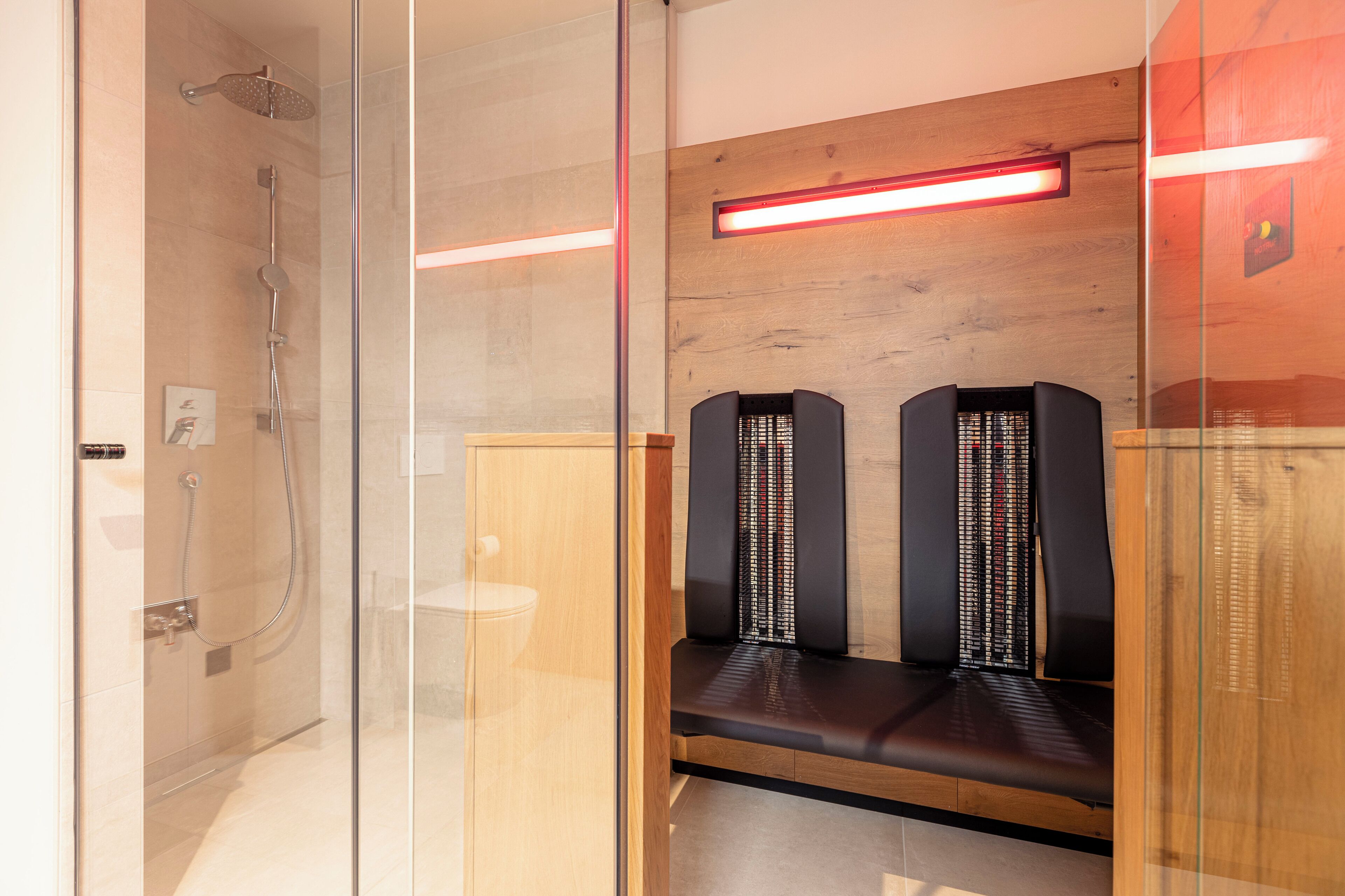 A modern bathroom with a glass-enclosed shower, wooden bench seating, and a red under-cabinet light.