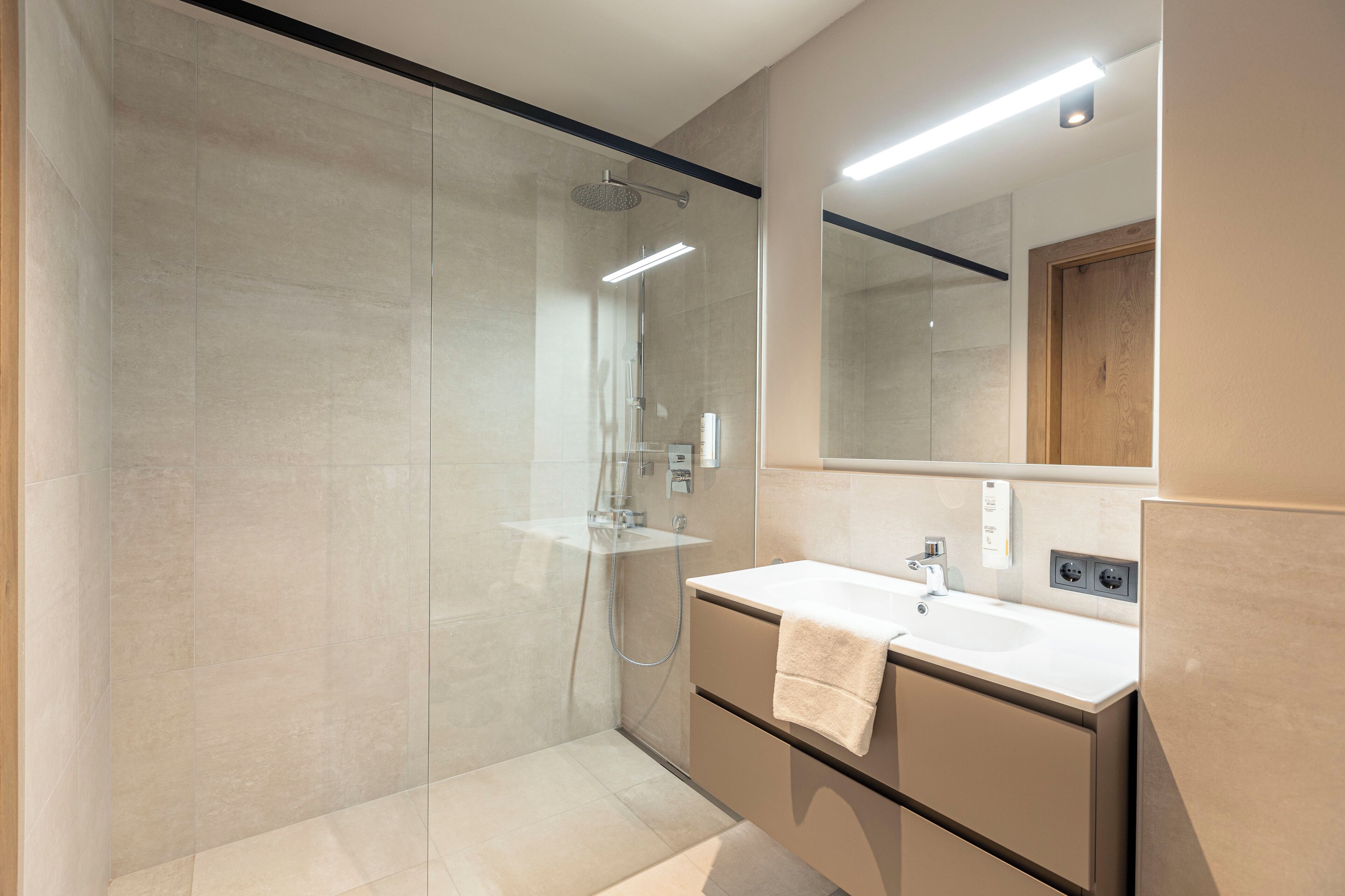 A modern bathroom with a glass-enclosed shower, a vanity with a sink, and a mirror.