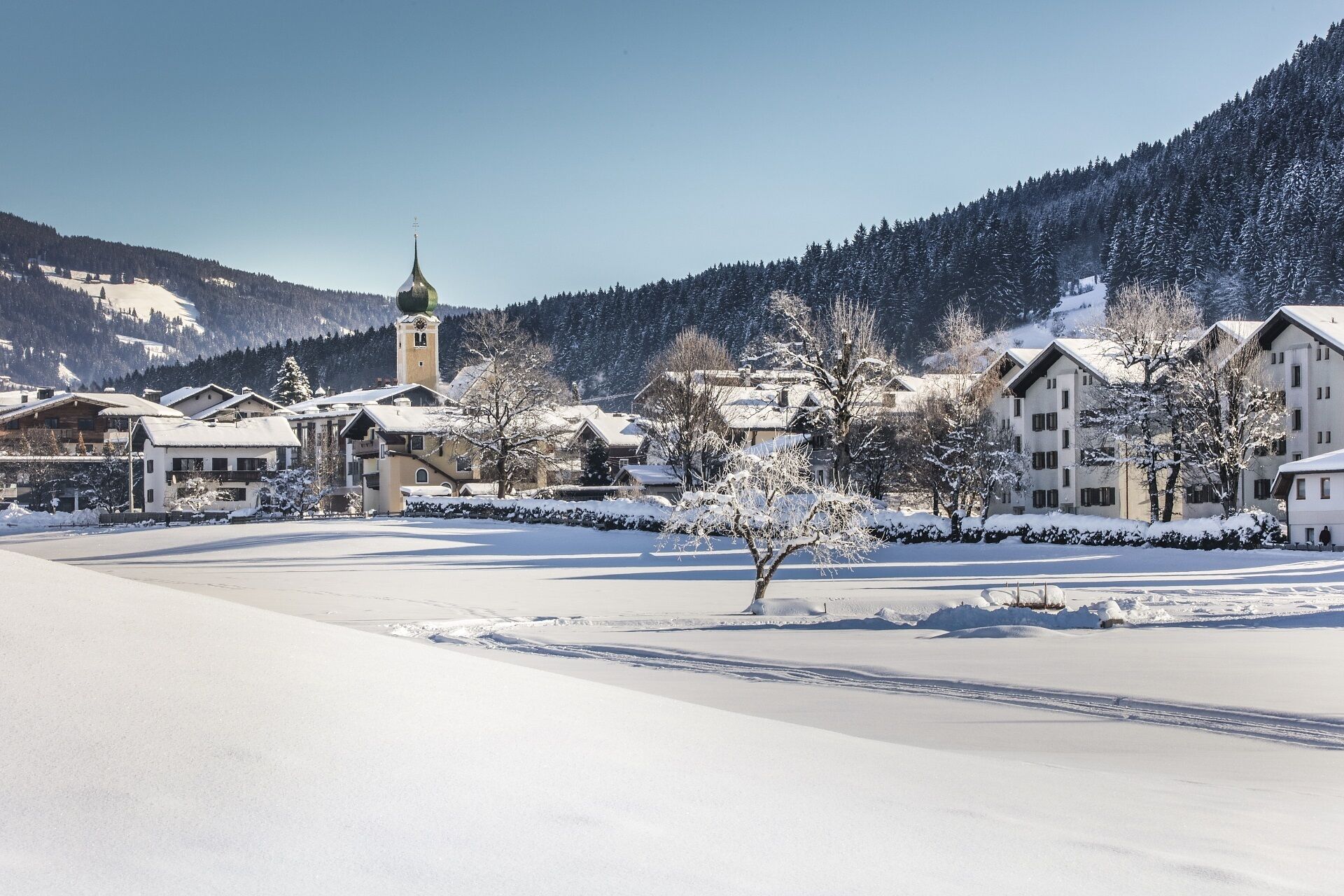 A snow-covered village with traditional buildings, a church tower, and a clear sky.