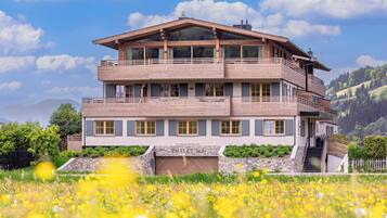 Ein mehrstöckiges Holzhaus mit Balkonen, eingebettet in ein üppiges, grünes Feld mit gelben Blumen.