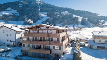 Ein mehrstöckiges Hotel mit Holzfassade, gelegen in einer verschneiten Bergregion mit Skipisten im Hintergrund.