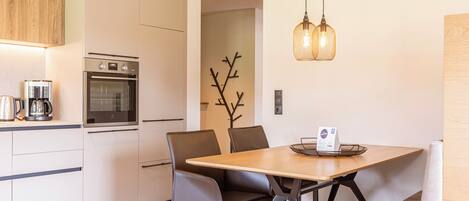 A modern kitchen with a built-in oven, a coffee maker, and a dining area with a wooden table and chairs.