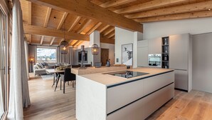 A modern kitchen with a central island, wooden beams on the ceiling, and a dining area with a sofa and chairs. - Chalet 149 Westendorf by ALPS RESORTS (Westendorf)