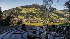 A circular stone water feature with a clear view of a town and mountains in the background. - Chalet 149 Westendorf by ALPS RESORTS (Westendorf)
