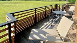 A wooden deck with outdoor furniture overlooking a green field and mountains. - Chalet 149 Westendorf by ALPS RESORTS (Westendorf)