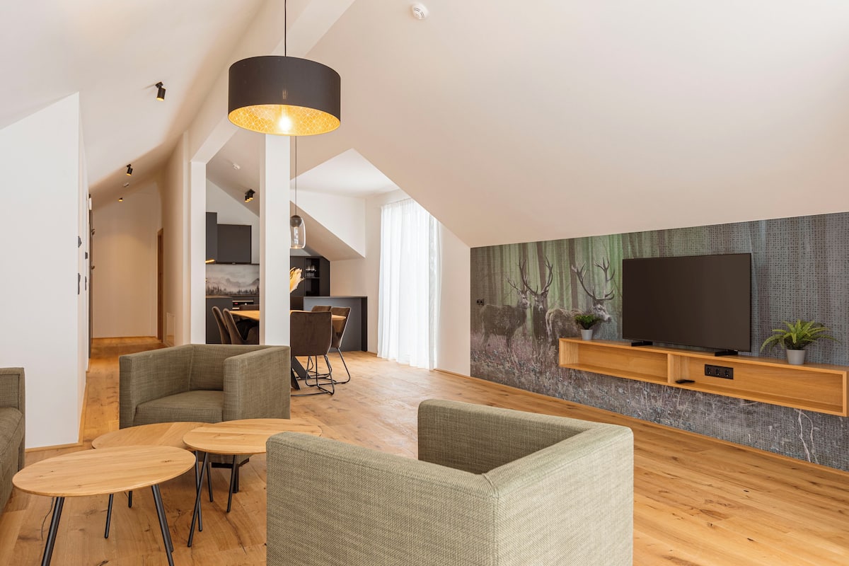 A modern living room with a flat-screen TV, wooden flooring, and green upholstered chairs.