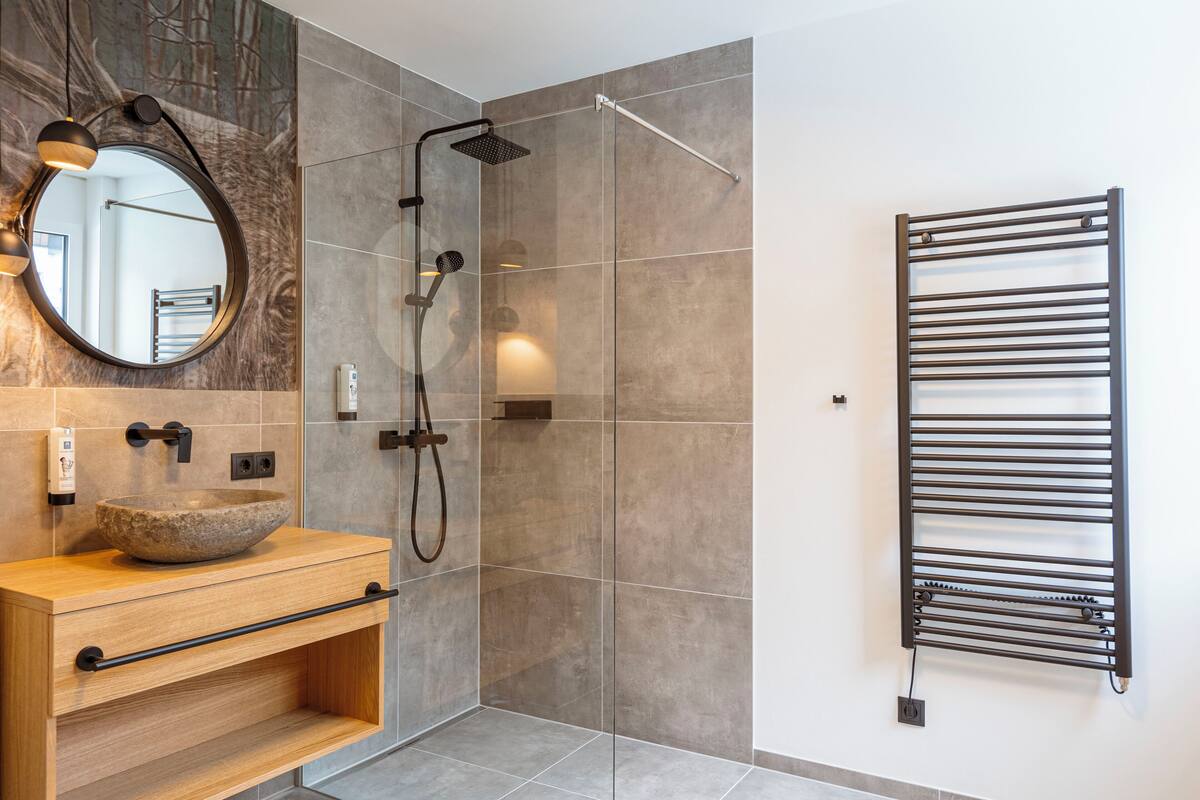 A modern bathroom with a stone sink, a handheld showerhead, and a towel rack.
