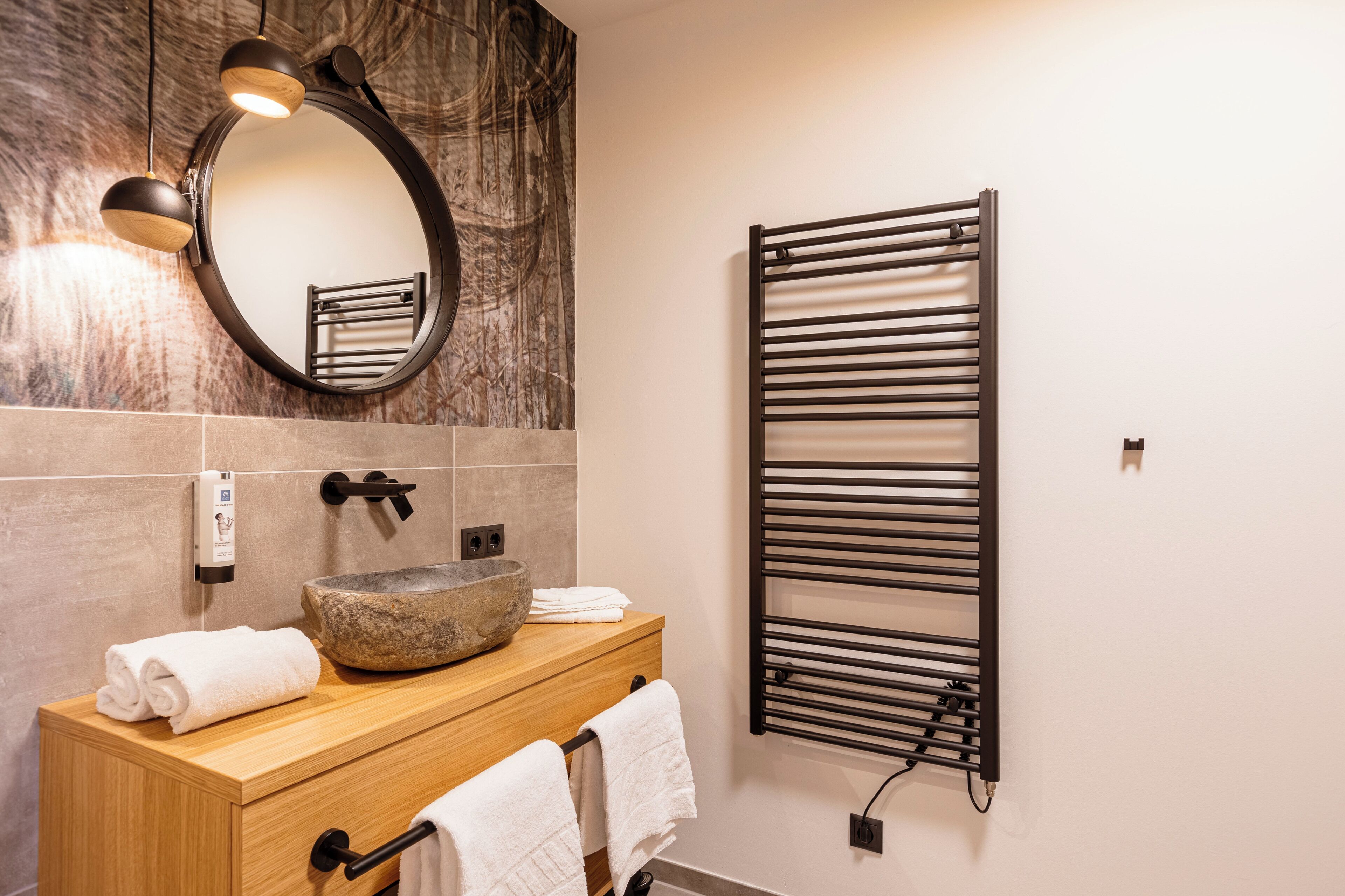Une salle de bain moderne avec un meuble-lavabo en bois, un lavabo en pierre, un porte-serviettes, un sèche-serviettes et un mur en marbre.