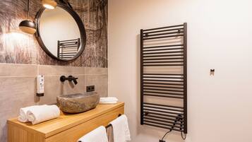Une salle de bain moderne avec un meuble-lavabo en bois, un lavabo en pierre, un porte-serviettes, un sèche-serviettes et un mur en marbre.