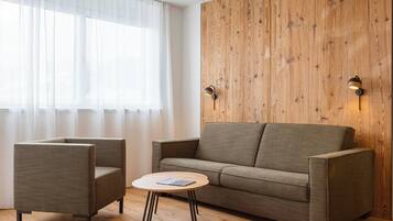 A modern living room with a wooden accent wall, a sofa, two armchairs, and a small round coffee table.