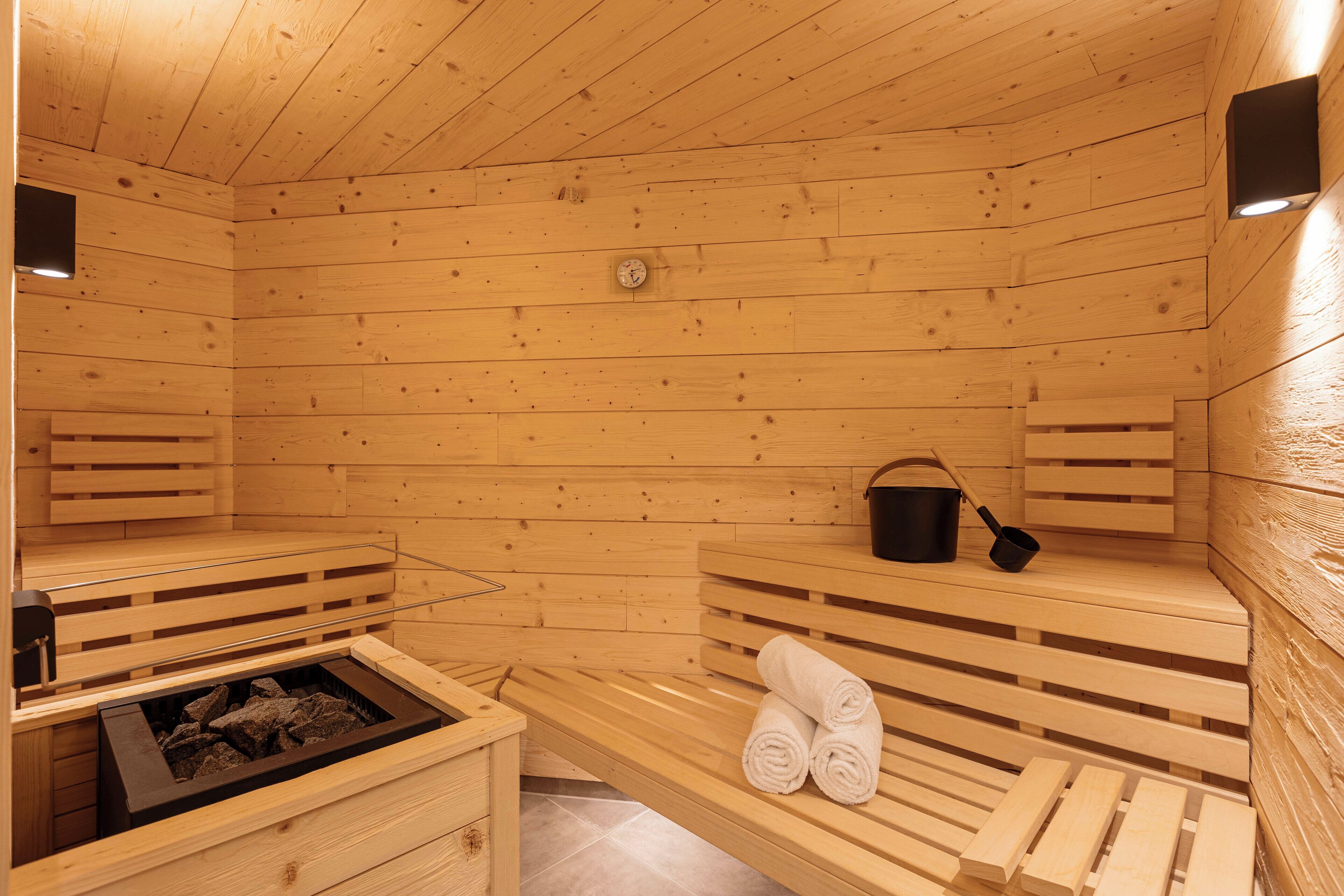 A wooden sauna with benches, a bench with towels, a bucket, and a heater.