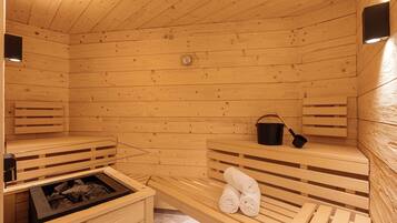 A wooden sauna with benches, a bench with towels, a bucket, and a heater.