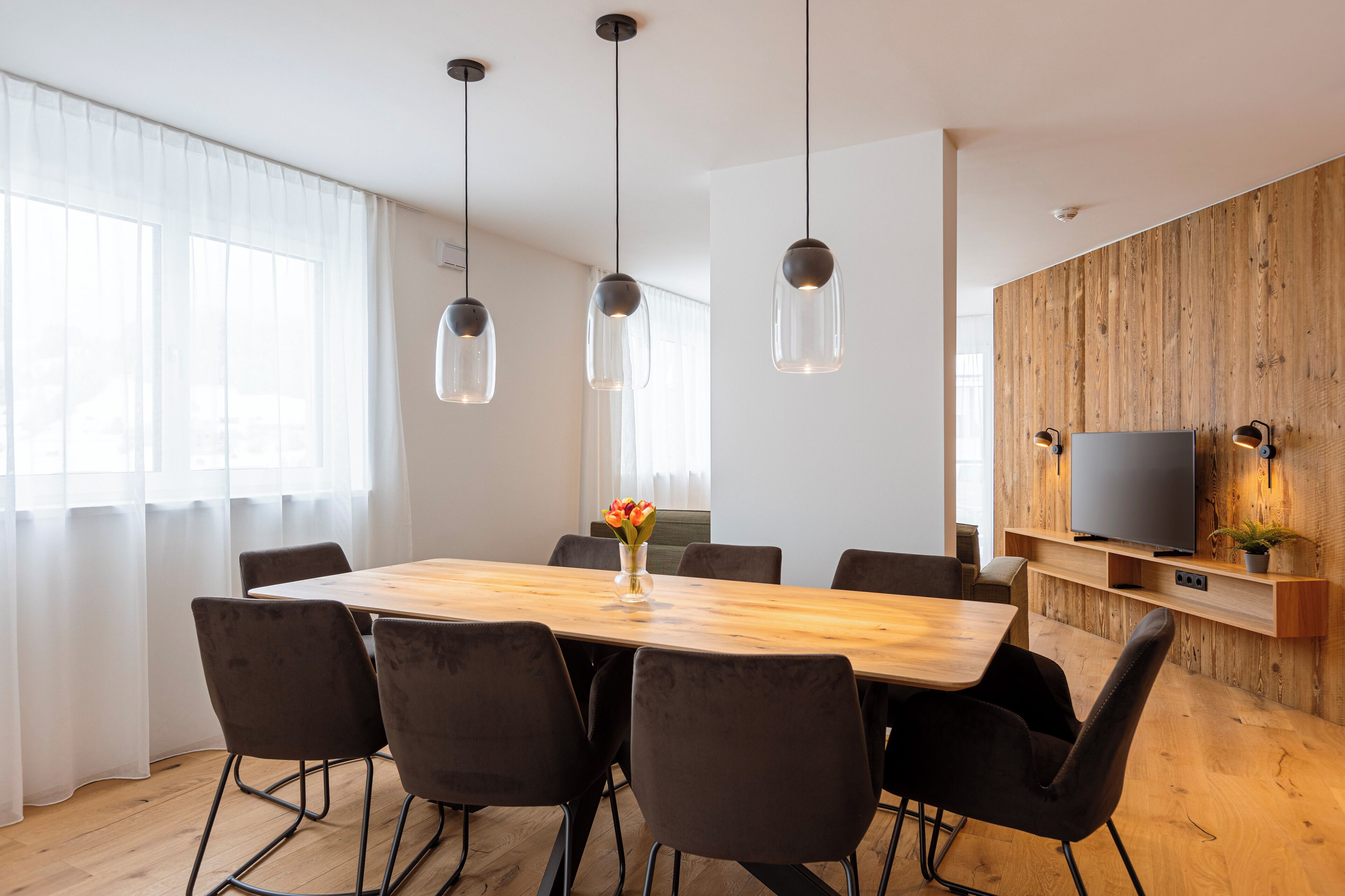 A modern dining area with a wooden table, black chairs, and pendant lights.