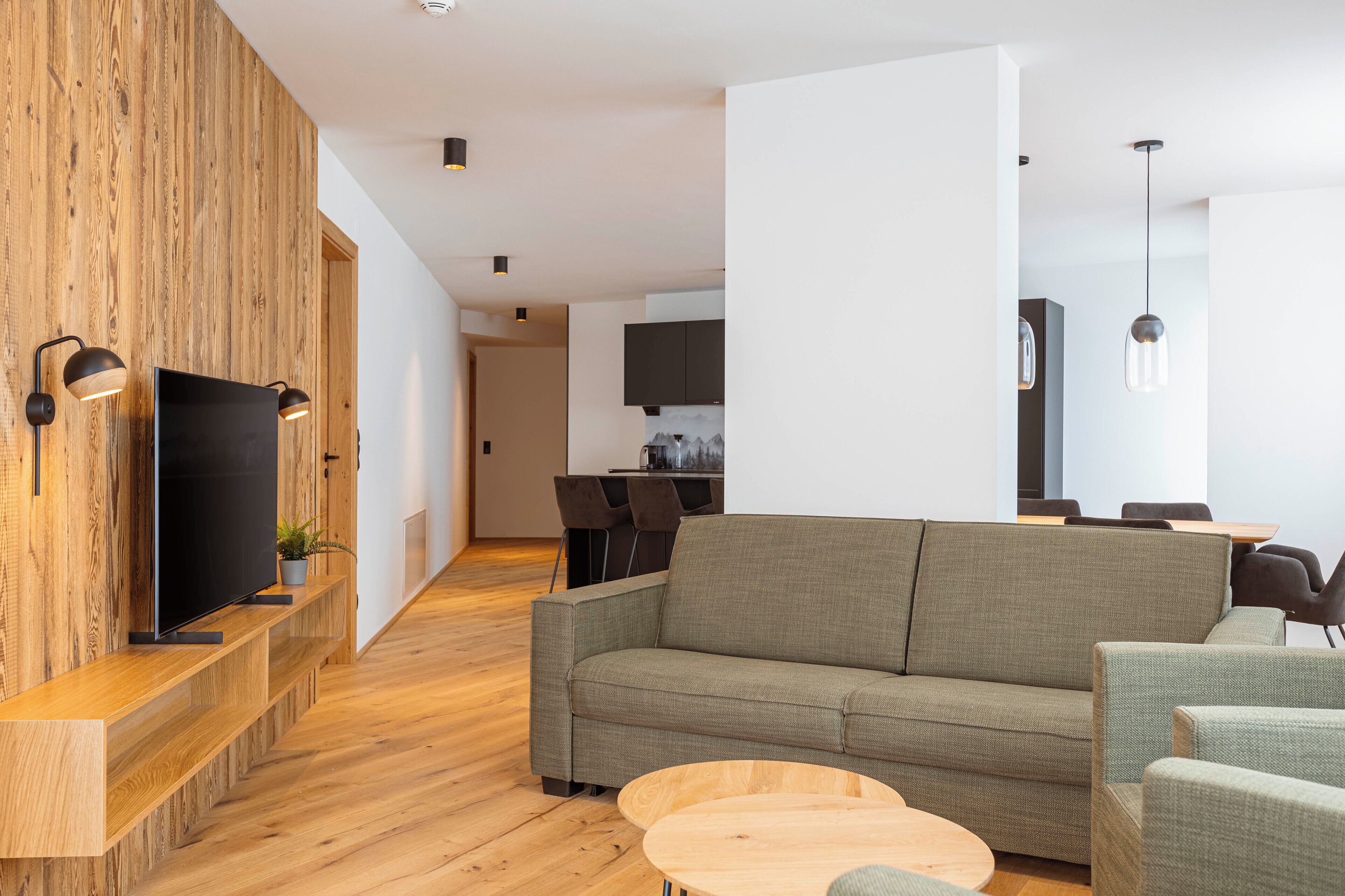 A modern living room with a wooden accent wall, a flat-screen TV, a grey sofa, and a wooden coffee table.