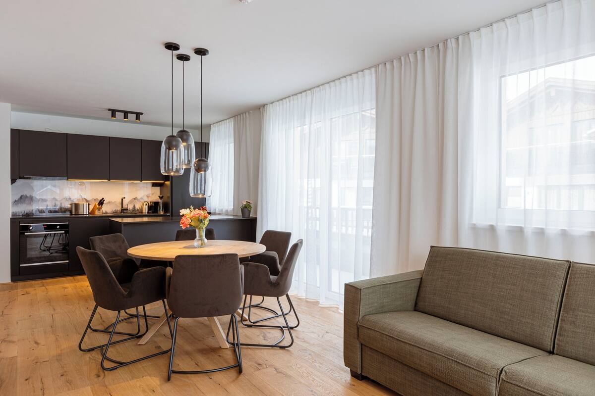 A modern kitchen with dark cabinets, a wooden dining table with chairs, and pendant lighting.