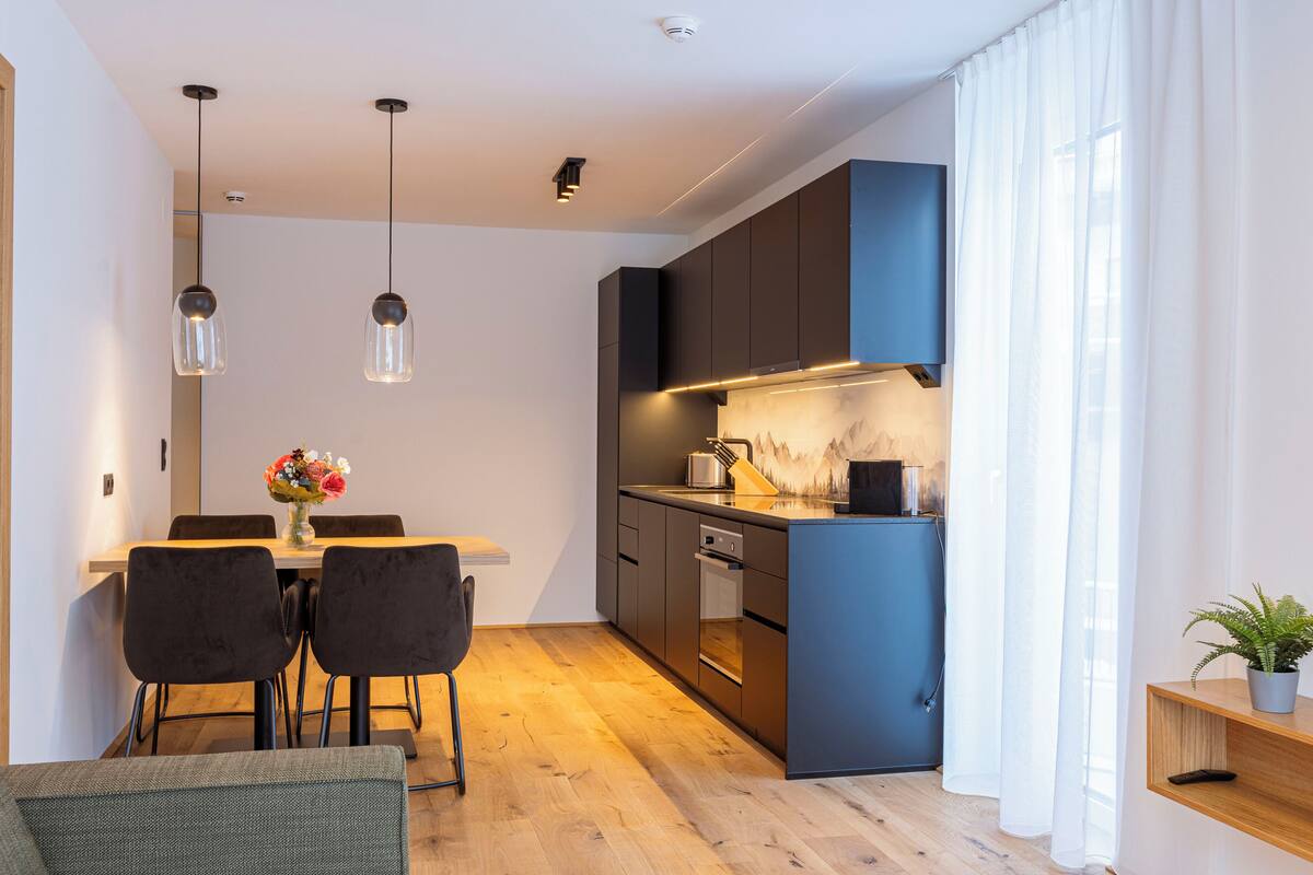 A modern kitchen with dark cabinets, a wooden dining table, and pendant lights.