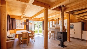 A spacious wooden cabin with a dining area, kitchen, and a large window providing natural light. - Feriendorf Murau by ALPS RESORTS (Murau)