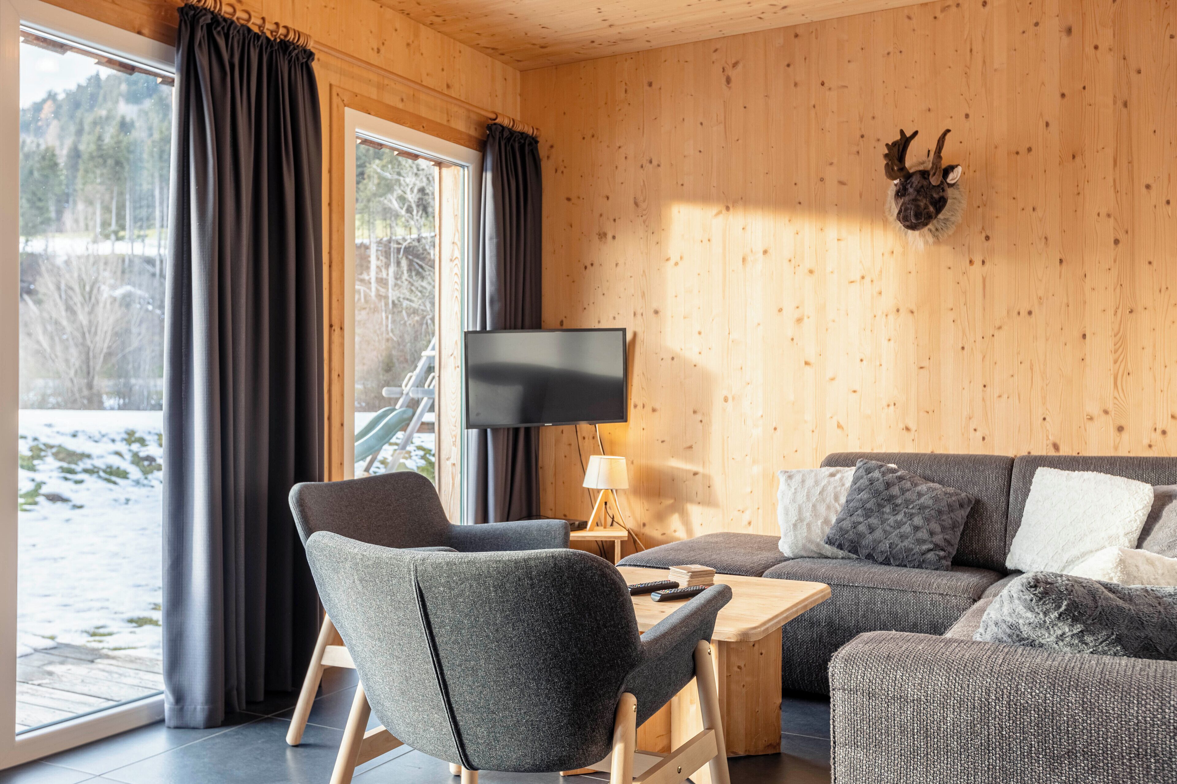 A cozy room with a wooden interior, a flat-screen TV, a sofa, and a chair.