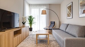 A modern living room with a flat-screen TV, wooden entertainment unit, grey sofa, and a coffee table. - King Apartamenty Galaxy (Szczecin)