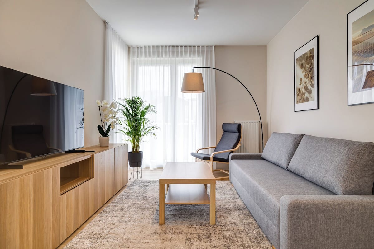 A modern living room with a flat-screen TV, wooden entertainment unit, grey sofa, and a coffee table.