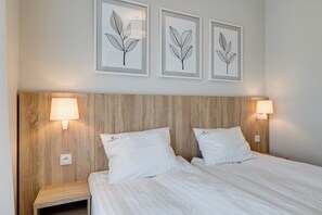 A neatly made bed with white linens, two bedside lamps, and a wooden headboard.