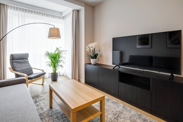 Una sala de estar moderna con un sofá, una mesa de centro de madera, una planta en maceta, una lámpara de pie, un televisor y un mueble multimedia de color oscuro.