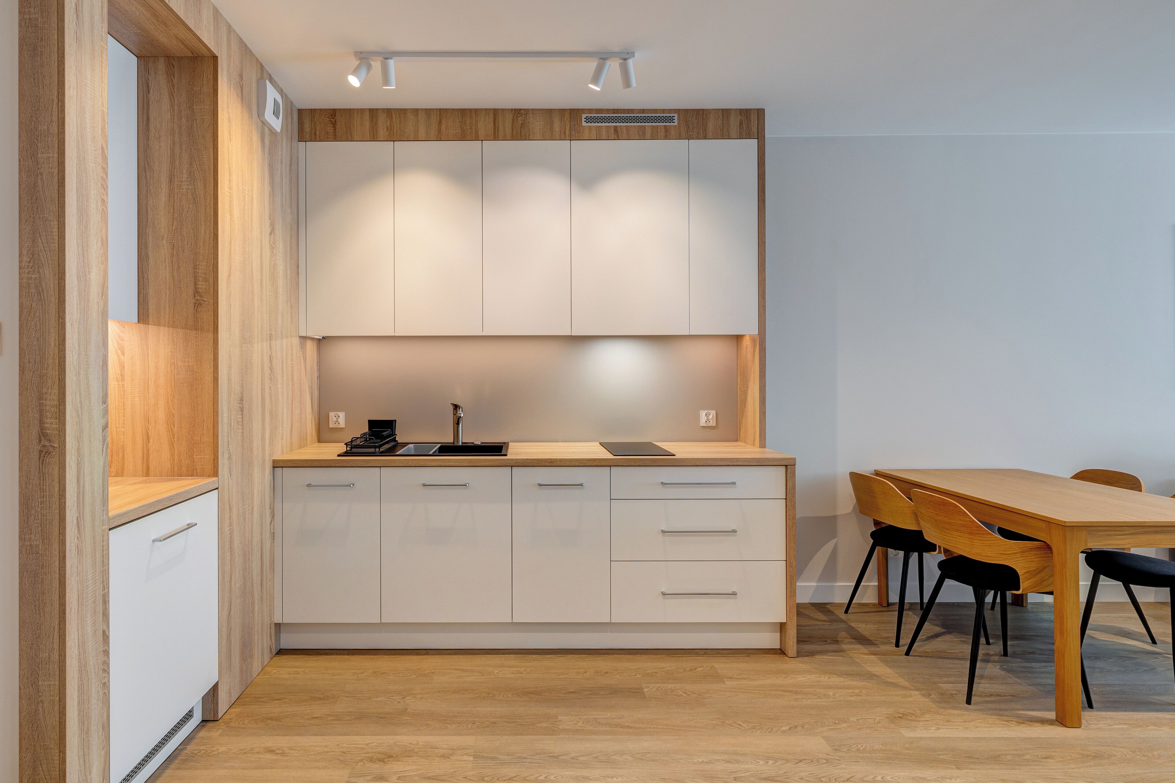 A modern kitchen with white cabinets, a wooden countertop, and a dining area with a wooden table and chairs.