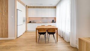 A modern kitchen with white cabinets, a wooden dining table, and chairs. - King Apartamenty Galaxy (Szczecin)