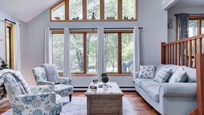 A living room with a sofa, armchairs, a coffee table, and large windows offering a view of trees. - Hot Tub, Lake, and LOCATION! Fall Hiking, Adventures and Relaxation (Albrightsville)