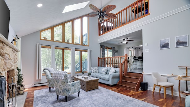 A spacious living room with a fireplace, a large window, a ceiling fan, and a staircase leading to an upper level. - Hot Tub, Lake, and LOCATION! Fall Hiking, Adventures and Relaxation (Albrightsville)