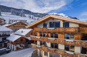 A multi-story wooden chalet with balconies, set against a snowy mountain backdrop.