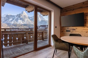 A room with a wooden balcony, a dining table with chairs, and a flat-screen TV mounted on the wall.