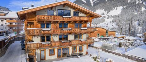 A multi-story wooden building with balconies, surrounded by snow-covered mountains.
