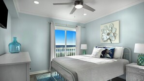 Une chambre à coucher comprenant un lit, une table de chevet, une commode, un ventilateur de plafond et une fenêtre avec des rideaux.