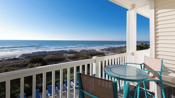 Un balcon avec une table et des chaises en verre donnant sur une plage.