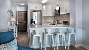 Une cuisine moderne avec des meubles blancs, un îlot central doté de tabourets, un four à micro-ondes et un réfrigérateur.