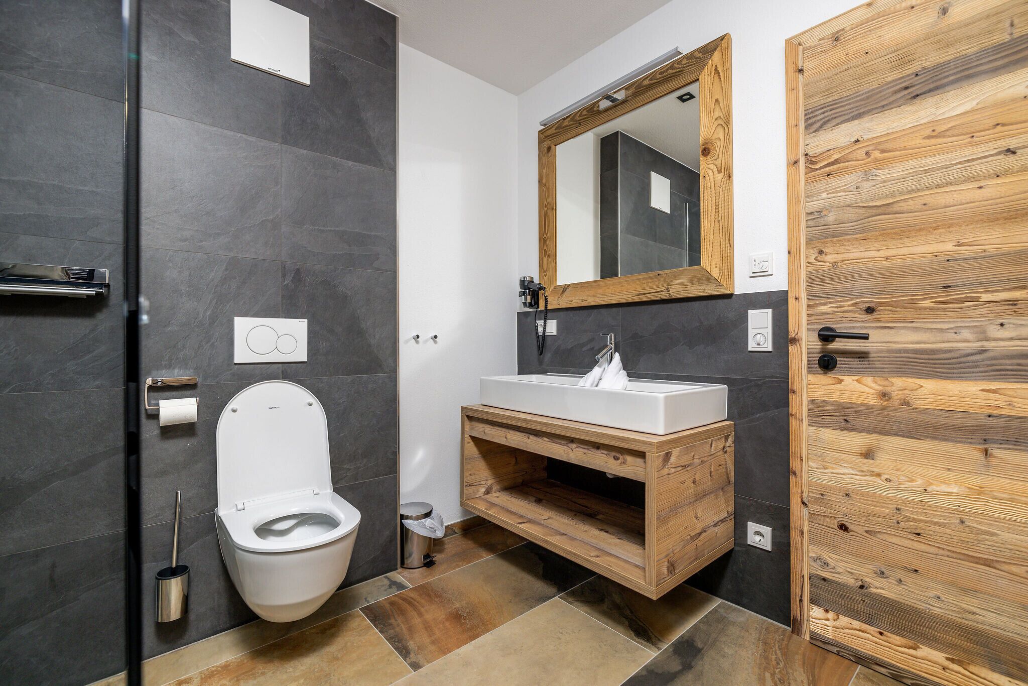 Un baño moderno con tocador de madera, inodoro blanco y un espejo grande.
