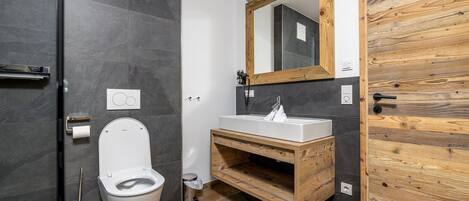 Un baño moderno con tocador de madera, inodoro blanco y un espejo grande.