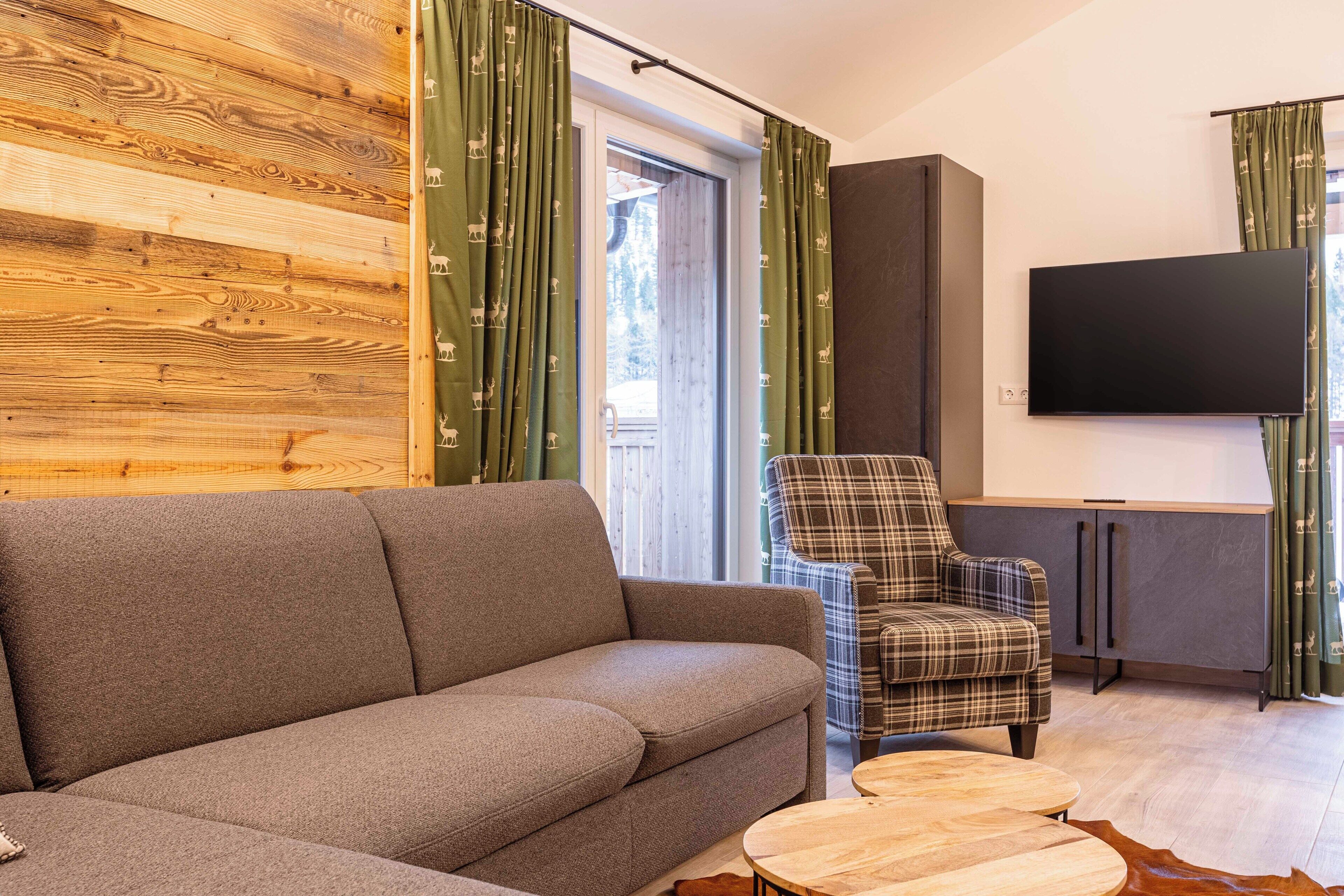 Un salon moderne avec un canapé, un fauteuil à motifs, un téléviseur à écran plat et un mur en bois.