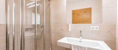 Un baño moderno con cabina de ducha de vidrio, un lavabo blanco y un panel de madera sobre el espejo.