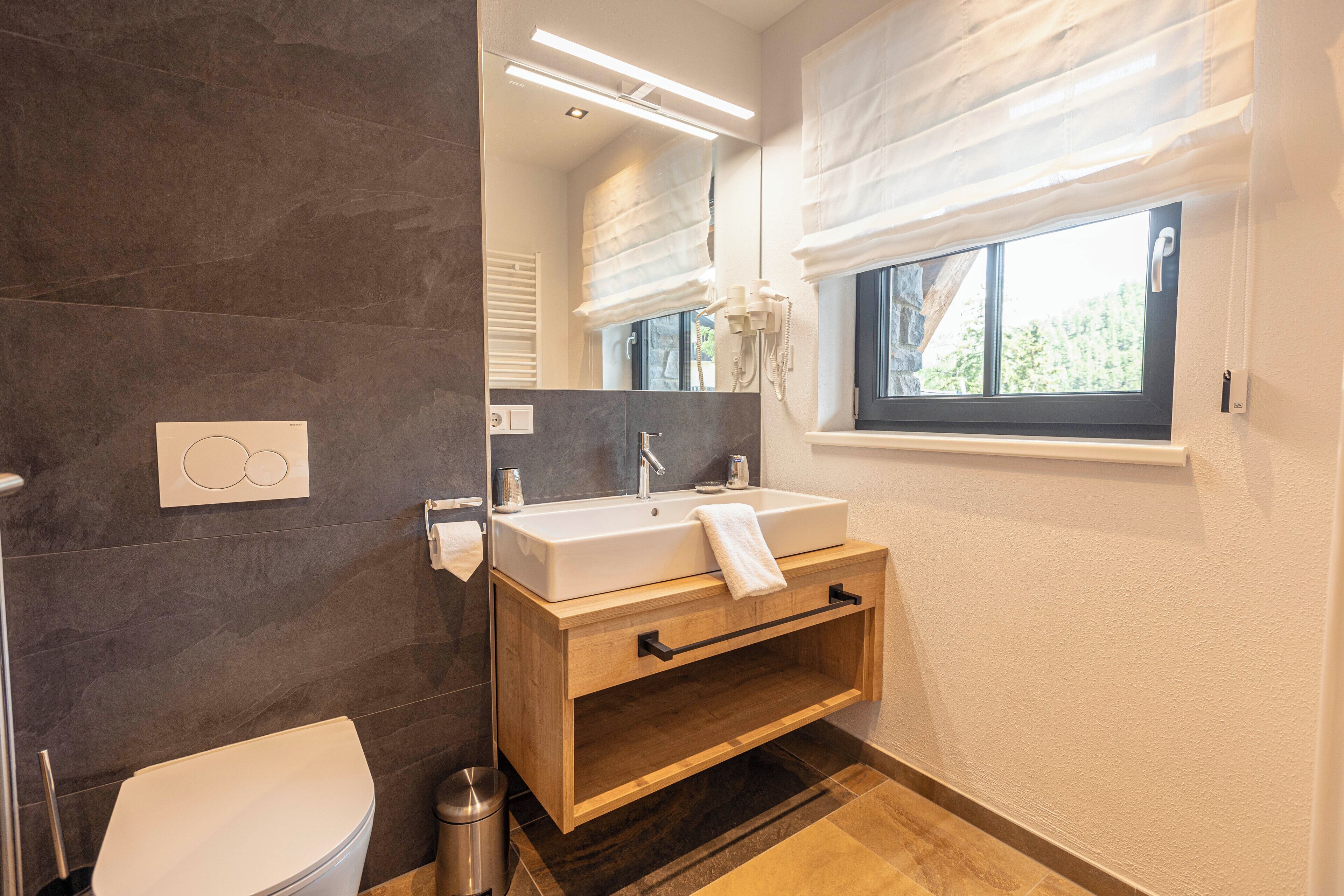 Ein modernes Badezimmer mit Toilette, einem Holzkonsolenunterschrank mit Waschbecken und einem großen Spiegel.