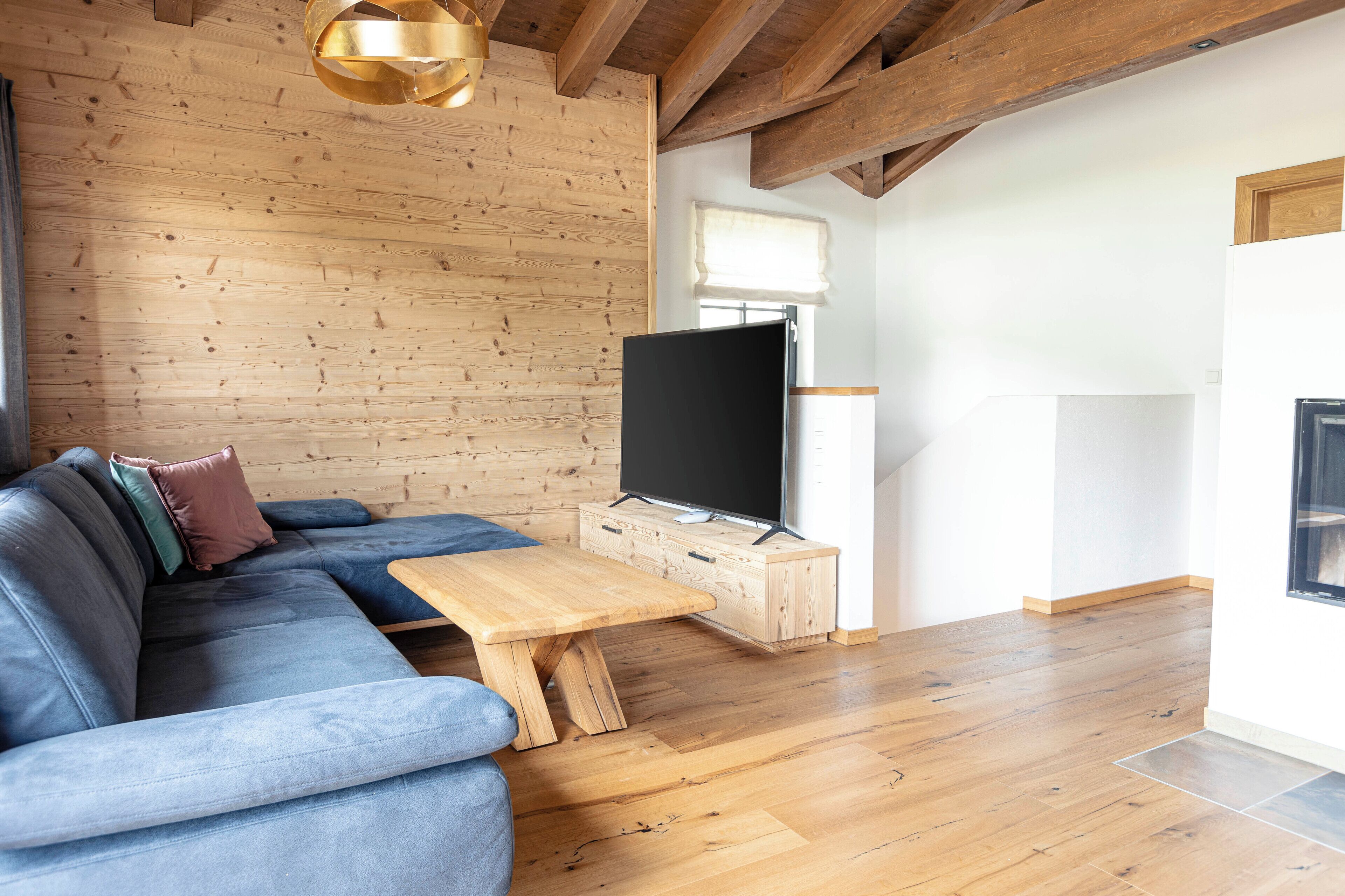 Ein modernes Wohnzimmer mit Holzboden, einem blauen Sofa, einem Couchtisch aus Holz und einem Flachbildfernseher auf einer Holzkommode.