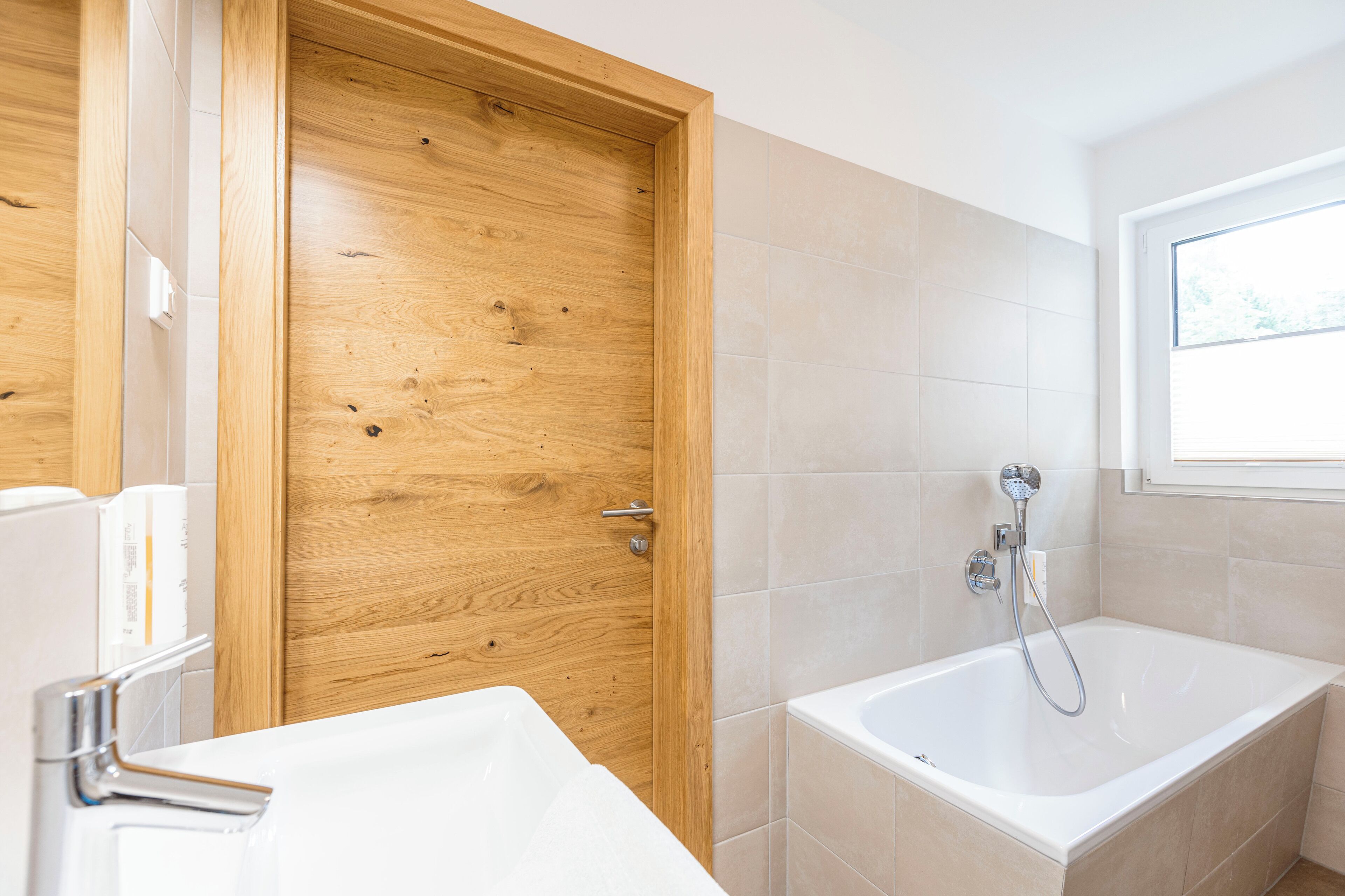 Un baño moderno con puerta de madera, una bañera y un ventanal que deja entrar luz natural.