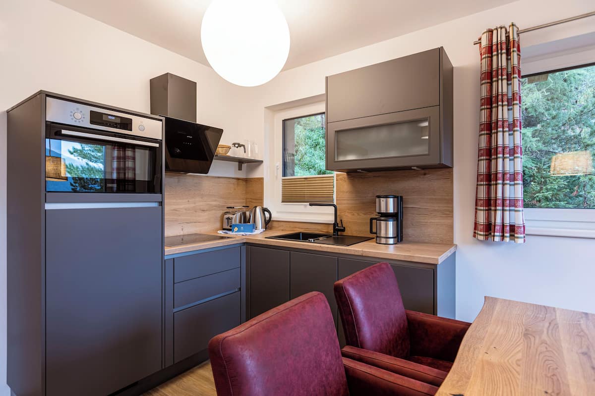 A compact kitchen with modern appliances, a dining area with a wooden table, and a view of greenery through the window.