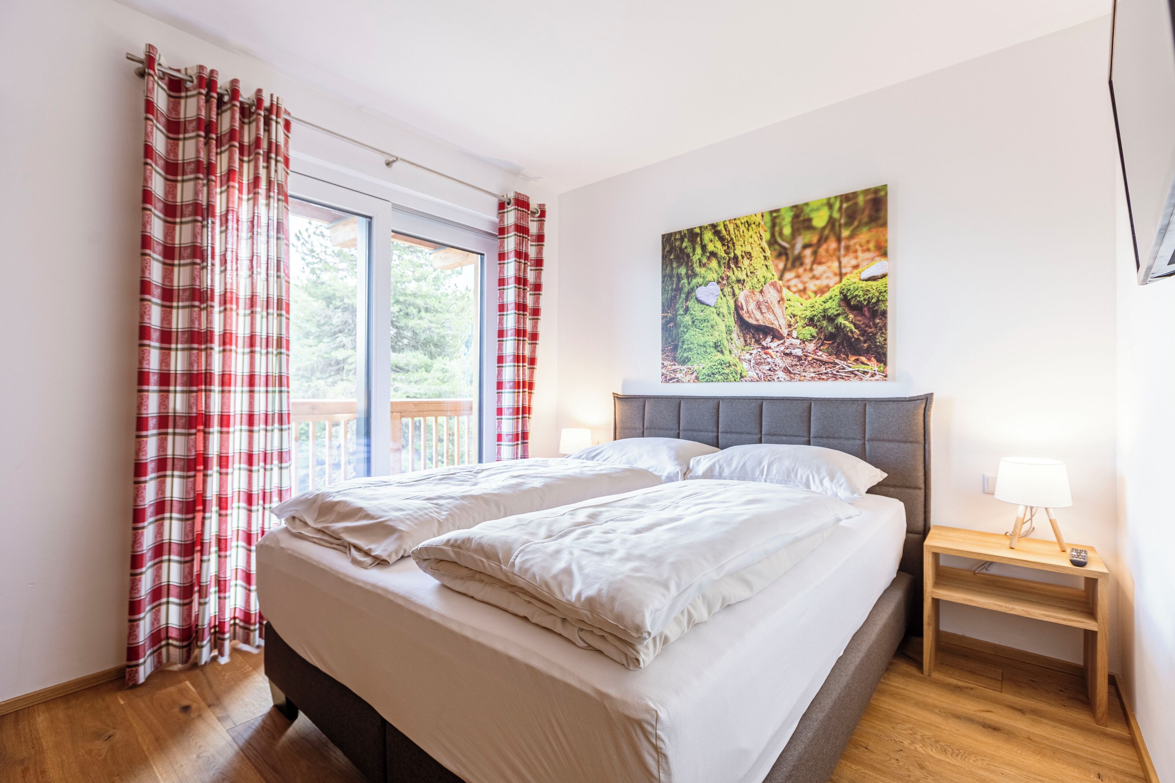 Een slaapkamer met een bed, nachtkastje, raam met gordijnen en een schilderij aan de muur.