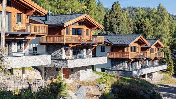 A multi-story wooden chalet with balconies, stone foundations, and a forest backdrop. - Turrach Lodges by ALPS RESORTS (Stadl-Predlitz)