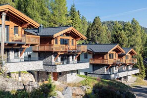 A multi-story wooden chalet with balconies, stone foundations, and a forest backdrop. - Turrach Lodges by ALPS RESORTS (Stadl-Predlitz)