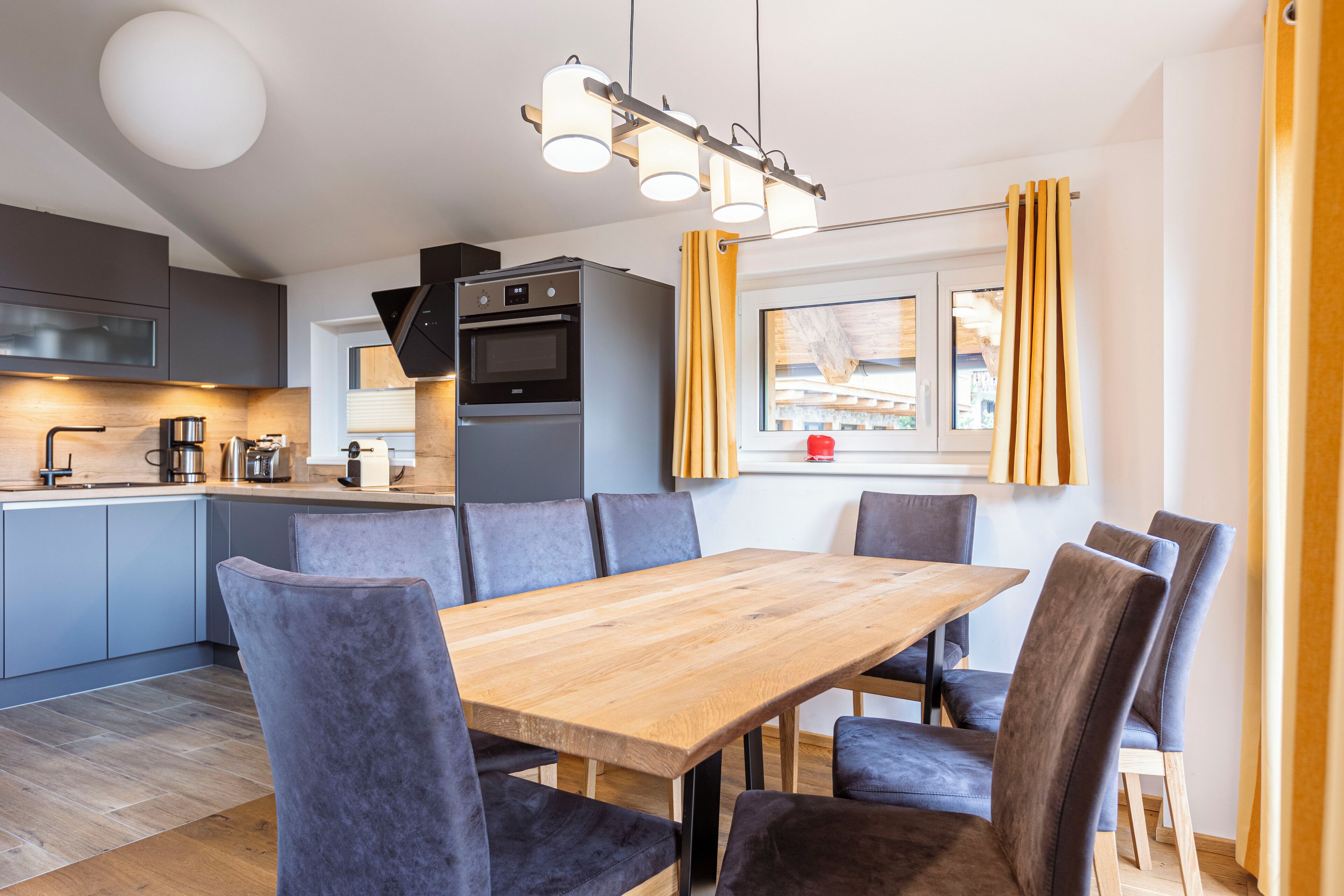 A modern kitchen with grey cabinets, a wooden dining table, and grey upholstered chairs.