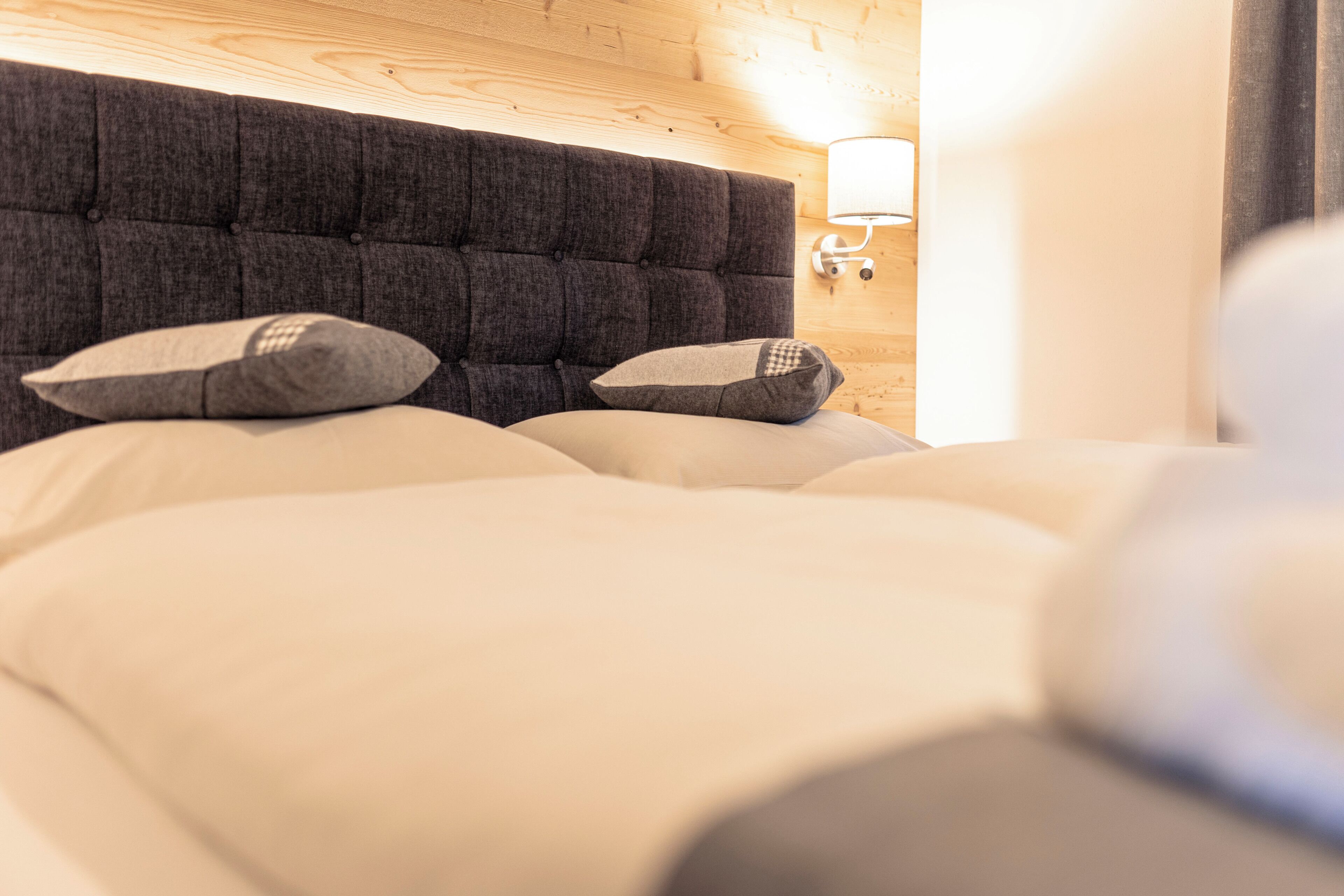Una cama con cabecera capitonada, dos almohadas y una lámpara de noche.