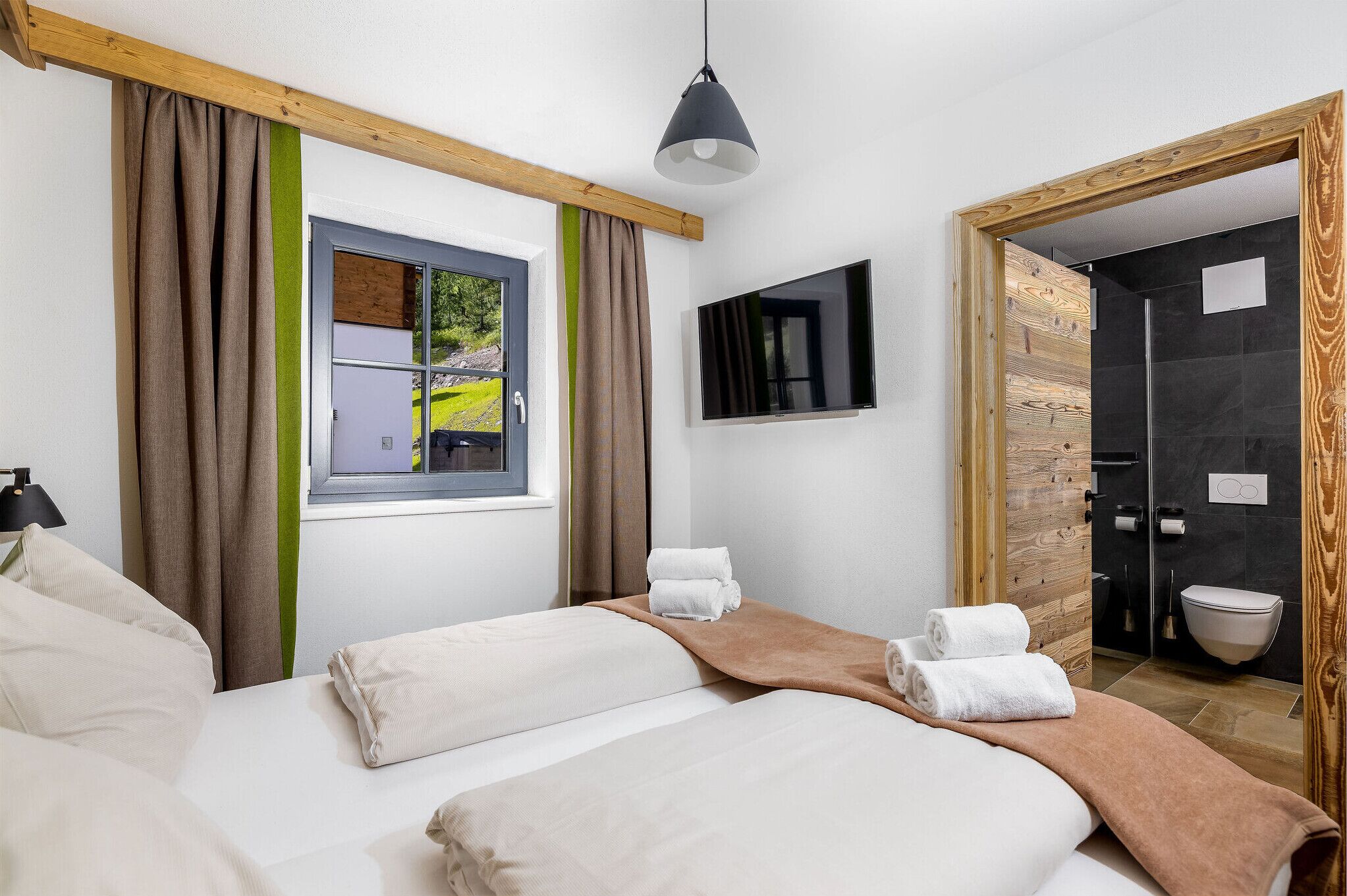 A hotel room with a bed, a window with curtains, a TV, and a bathroom visible through an open door.